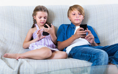 Two kids looking to smartphones on sofa