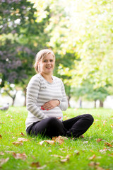 Happy and young pregnant woman in park in summer