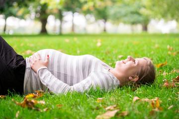 Happy and young pregnant woman in park in summer