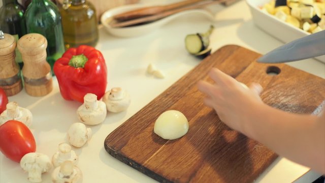 Female hands slicing bow vegetables on kitchen board close up