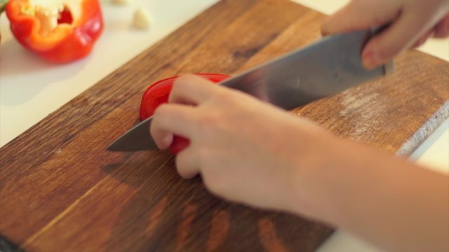 Female hands slicing red pepper vegetables on kitchen board close up