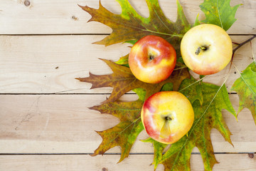 Red apples and autumn yellow maple leaves on a wooden table, close up, selective focus