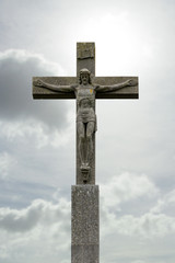 stone crucifix with Jesus Christ before cloudy sky