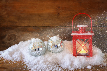 christmas background with red lantern, bauble and snow over wooden background. glitter overlay