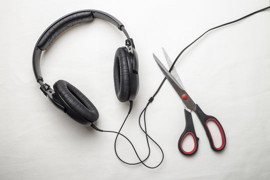Scissors cut the wire from the headphones, and thus stop the very loud illegal pirated music on a white background