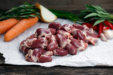  Raw Duck hearts on crumpled paper, decorated with greens and vegetables. on old  wooden table
