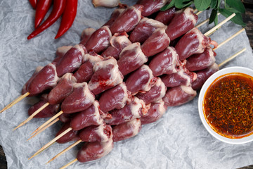 Ready to cook Duck Heart stringed on skewers BBQ with hot sauce and chili pepper. decorated with greens and vegetables.  background.