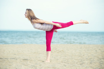 Young lady practicing yoga. Workout near ocean sea coast.