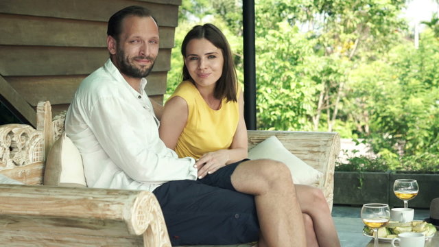 Portrait of happy, young couple sitting on wooden sofa on terrace
