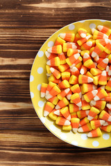 Halloween candy corns in plate on brown wooden background