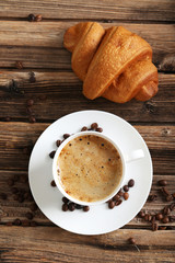 Delicious croissant with cup of coffee on brown wooden backgroun