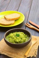 Rustic bowl of homemade zucchini and parsley spread garnished with fresh parsley leaf, slices of wholegrain bread in the back, photographed with natural light (Selective Focus, Focus on the leaf)