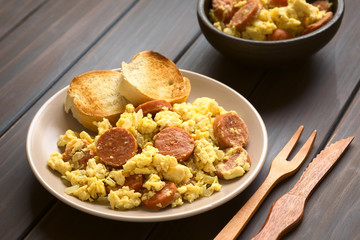 Scrambled eggs made with chorizo slices and onion on plate with toasted baguette slices, photographed with natural light (Selective Focus, Focus one third onto the plate)