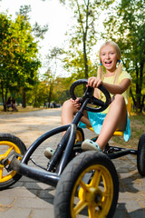 Beautiful happy little girl riding toy car in summer city park