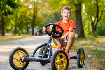 happy smiling boy driving a toy car outdoor in the park