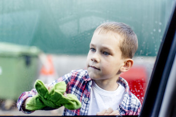 boy diligently washes a window in the car. Boy biting his lip carefully washes a window in the car outside