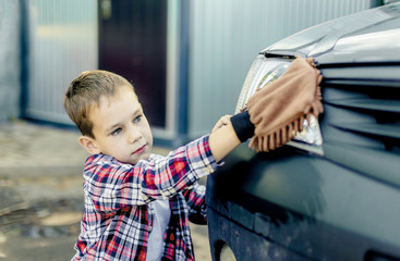 child wipes car headlights mitten. boy washes the car special soft mitten worn on the arm
