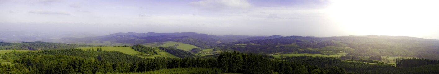 Panorama with hills, forests, sky and sun shine