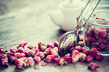 Rose buds tea, tea strainer closeup, glass jar and teapot on bac