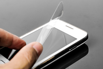 hand laying scratch protective film on a smartphone - obrazy, fototapety, plakaty