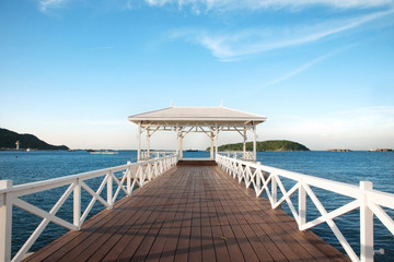 Fototapeta na wymiar Beautiful white wooden bridge laying toward the sea with blue sky at the beach in Thailand.