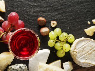 Different types of cheeses with wine glass and fruits.
