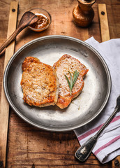 Two roasted pork steaks on rustic metal plate on wooden background