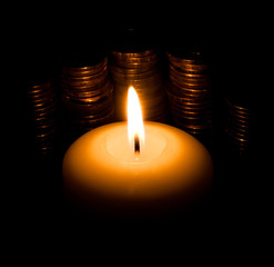 Burning candle in the night on a background of gold coins