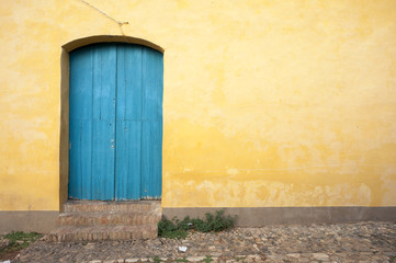 Simple brightly painted blue door in a smooth yellow ochre stucco wall on a cobblestone street in Trinidad, Cuba