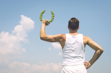 Athlete in old fashioned white uniform holding laurel wreath against sunny blue sky