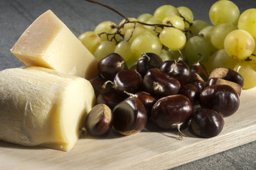 Chesse, chestnuts and grapes on cutting board