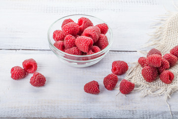 Ripe sweet raspberries in bowl on white wooden table