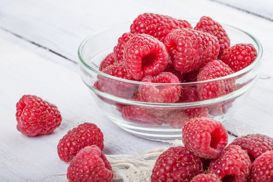 Ripe sweet raspberries in bowl on white wooden table