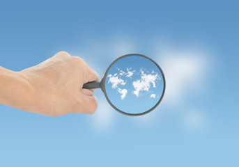 Hand holding magnifying on blue sky clouds world map background
