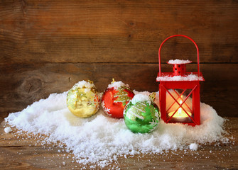 christmas background with red lantern, bauble and snow over wooden background
