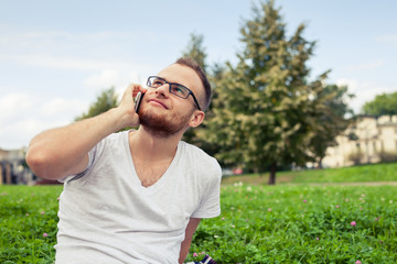 Naklejka na ściany i meble Bearded man sitting in park on blanket. He is using mobile phone.