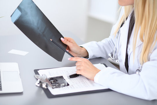 Close up of female doctor holding x-ray or roentgen image, sitting at the table