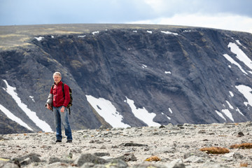 Fototapeta premium Caucasian hiker with a backpack standing on the mountain plateau and looking at camera, copy space