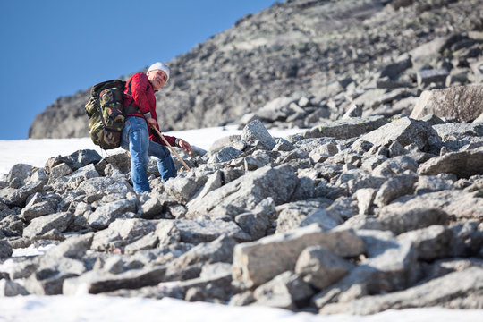 Mature Caucasian hiker climbing with backpack in steep slope mountains at summer season