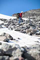 Fototapeta premium Mature Caucasian hiker standing on the top of mountain at steep stony slope, looking down