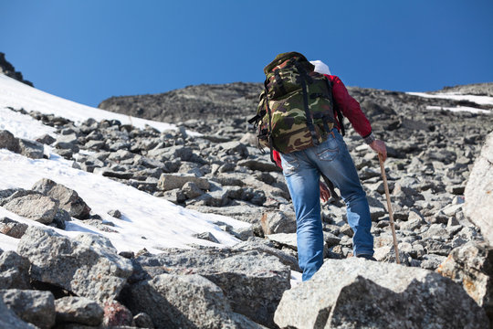 Rear view of hiker climbing on steep stony slope in mountains