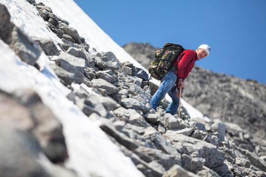 Mature man climbing in mountain at summer season, resting on steep slope