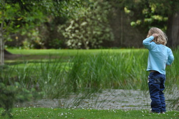 a blond child looks at a pond surrounded by nature