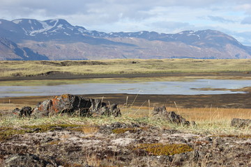 Widok na pasmo górskie w Islandii, u podnóża łąki o przebarwieniach i płytkie jezioro w porze...