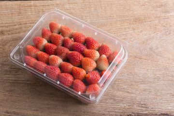 red ripe strawberry in plastic box of packaging on wood table