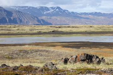 Widok na pasmo górskie w Islandii, u podnóża łąki o przebarwieniach i płytkie jezioro w porze jesiennej.