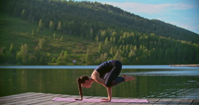Yoga professional performing crow pose and handstand on pier over lake 