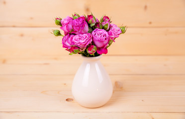 Pink roses in a vase on wooden background