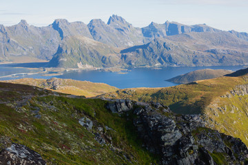 Beautiful Vibrant Norwegian Mountain Landscape from Ryten peak - famous mountain in Lofoten Islands, Moskenes municipality, Nordland with a view of Kvalvika beach, with hiking tourists and blue sky
