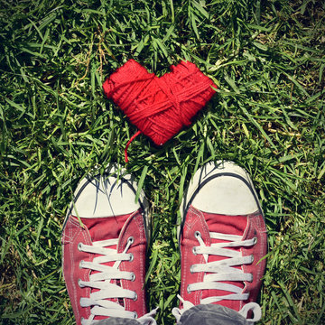 man feet and heart-shaped coil of red cord on the grass, vignett